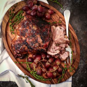 Braised Lamb Shoulder with Grapes and fresh thyme on a wood serving board.
