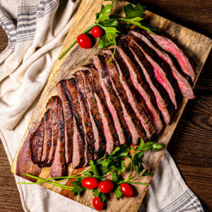 A sliced grilled flank steak on a wood cutting board.