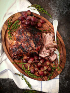 Braised Lamb Shoulder with Grapes and fresh thyme on a wood serving board.