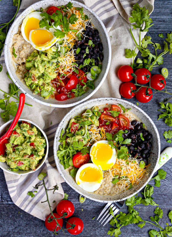 Two Mexican Breakfast Bowls with tomatoes, guac and cilantro scattered around.