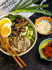 A bowl of ramen garnished and with an egg and sesame seeds and chopsticks laid across the bowl.