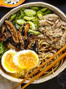 A bowl of Homemade Chicken Ramen with scallions alongside and chopsticks on the edge of the bowl.