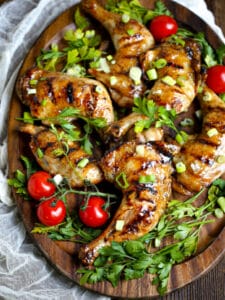 Honey Glazed Grilled Chicken Legs on an oval wood platter garnished with parsley and cherry tomatoes.