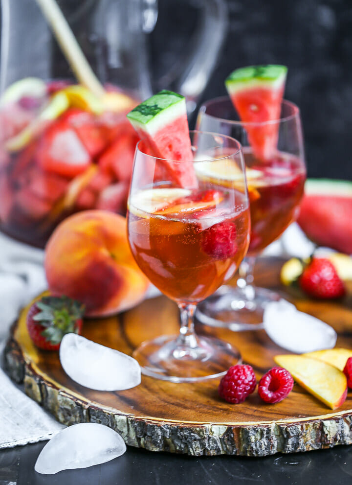 Two glasses of chilled Rosé Sangria served on a wood board with fruit scattered around.
