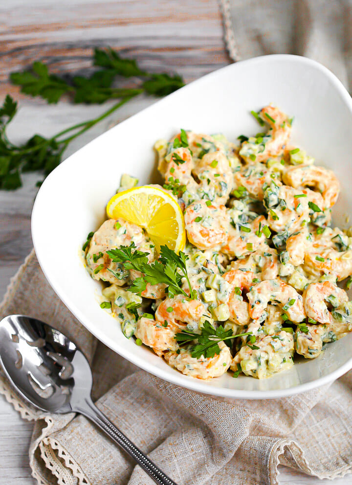 A bowl of creamy shrimp salad in a white bowl garnished with parsley and lemon.