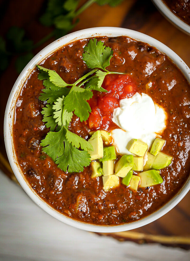 Overhead shot of Easy Black Bean Soup garnished with yogurt, avocado, salsa and spices.