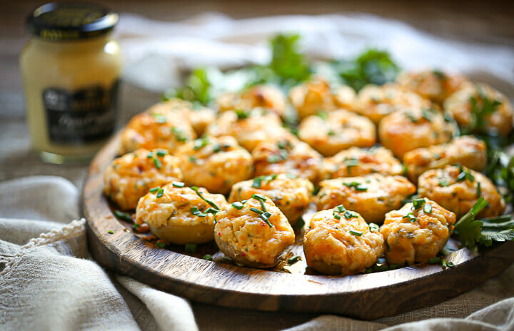 A serving plate of Mini Cheesy Twice-Baked Potatoes garnished wit herbs.