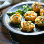 Close up of Mini Cheesy Twice-Baked Potatoes on a black plate garnished with herbs.