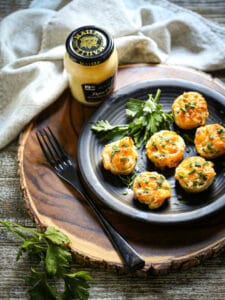 Mini Cheesy Twice-Baked Potatoes garnished with parsley with a jar of Maille mustard on the table.