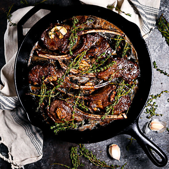Overhead shot of Pan Seared Lamb Chops with garlic and thyme scattered around.