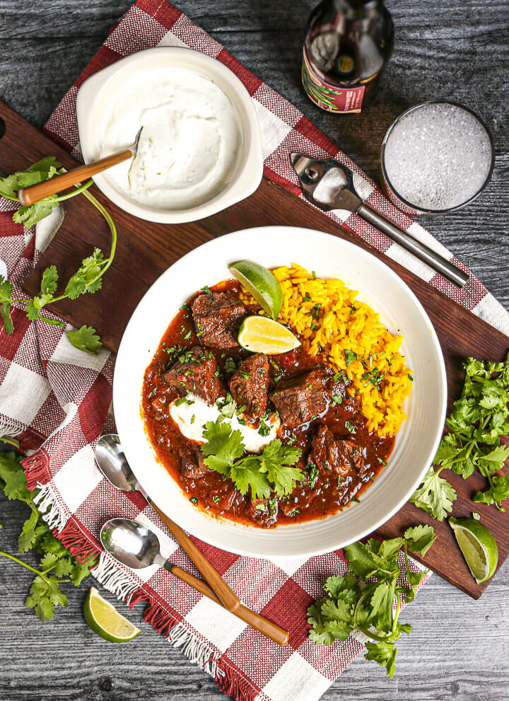 Overhead shot of a serving of Mexican Beef Stew served with yellow rice, lime crema and a beer.