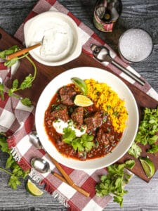 Overhead shot of a serving of Mexican Beef Stew served with yellow rice, lime crema and a beer.