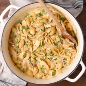 A pot of One Pot Creamy Chicken Pasta stirred with wooden spoon.