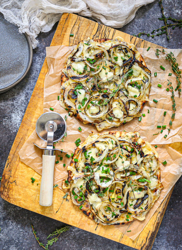 Grilled Onion and Swiss Flatbread on a parchment lined cutting board with a pizza cutter.