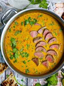 Coconut lamb curry in a saute pan with herbs and naan alongside.
