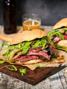 Two steak sandwiched on a wood board with a side of aioli on the table.