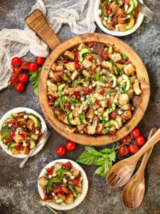 Overhead shot of Garden Vegetable and Pancetta Panzanella with some plated servings scattered around the table.