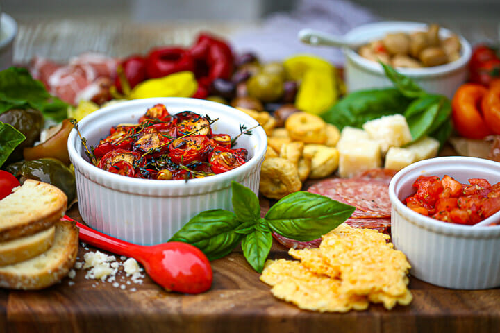 A bowl of roasted tomatoes on a served on an Italian grazing board.