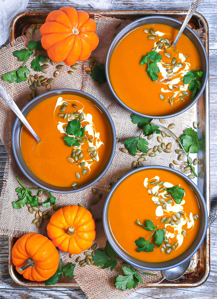 A tray of garnish pumpkin soups with garnished and mini pumpkins.