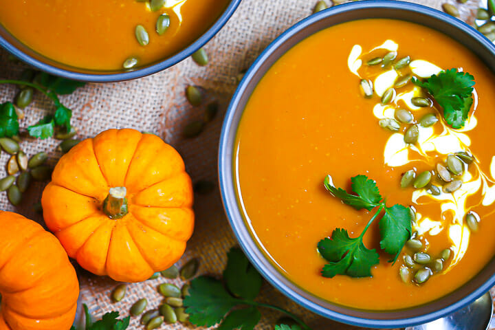 Close up of a bowl of Easy Curried Pumpkin Soup garnished with yogurt, pumpkin seeds and cilantro.