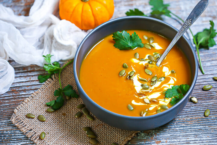 A bowl of pumpkin soup on a piece of burlap with pumpkin seeds scattered around.