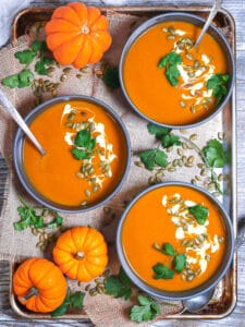 A tray of garnish pumpkin soups with garnished and mini pumpkins.