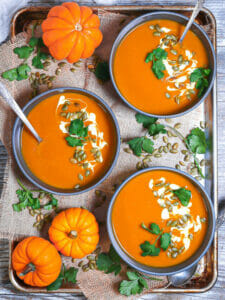 A tray of garnish pumpkin soups with garnished and mini pumpkins.