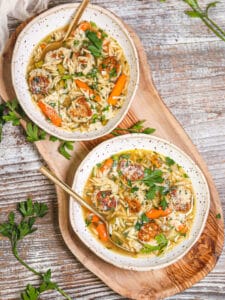 Overhead shot of two servings of chicken meatball soup on a wood serving tray.