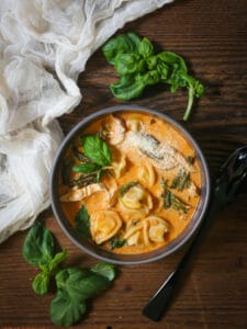 A bowl of hot tortellini soup ready to eat with a spoon alongside.