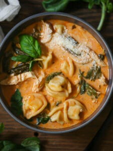 A bowl of hot tortellini soup ready to eat with a spoon alongside.