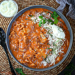 A serving of one pot lasagna soup in a gray bowl with a spoon and parmesan alongside.