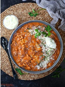 Overhead shot of a bowl of lasagna soup on a wooded beaded placemat.