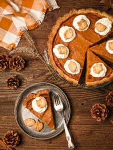 A slice of sweet potato pie with marshmallow whipped cream on a plate next to the pie.