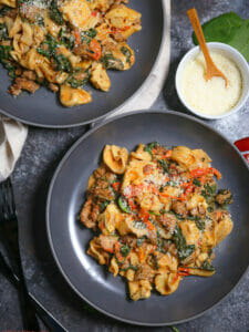 Overhead shot of two bowls and One Pot Creamy Sausage Tortellini with Spinach and Tomatoes with grated parmesan alongside.