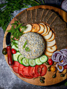 Overhead shot of Everything Bagel Smoked Salmon and Cream Cheese Ball on a platter with veggies, pumpernickel toasts and herbs.