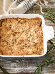 Roasted Cauliflower Gratin fresh out of the oven on a table with rosemary sprigs scattered around.