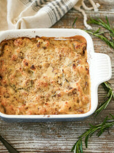 Roasted Cauliflower Gratin fresh out of the oven on a table with rosemary sprigs scattered around.