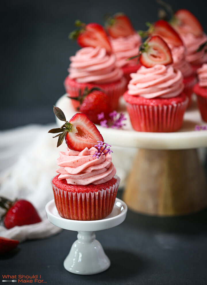 A strawberry cupcake on a mini cupcake stand with cupcakes in the background.