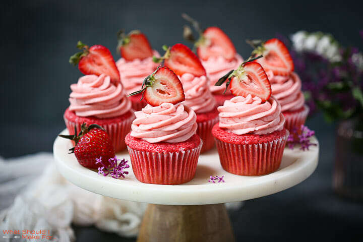 Strawberry cupcakes arranged on cake stand with flowers and strawberries.