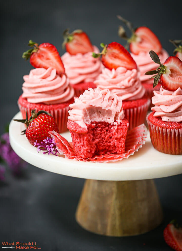 Strawberry cupcakes on a cake plate, one with a bite taken out.