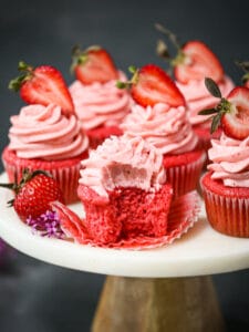 Strawberry cupcakes on a cake plate, one with a bite taken out.